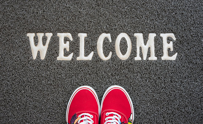 A pair of shoes on a welcome mat, representing a member welcome letter.