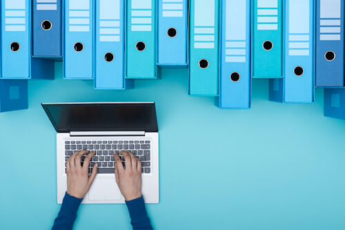 An association member types on a laptop facing a clean and artistic collection of blue filing binders that make up the association's database.