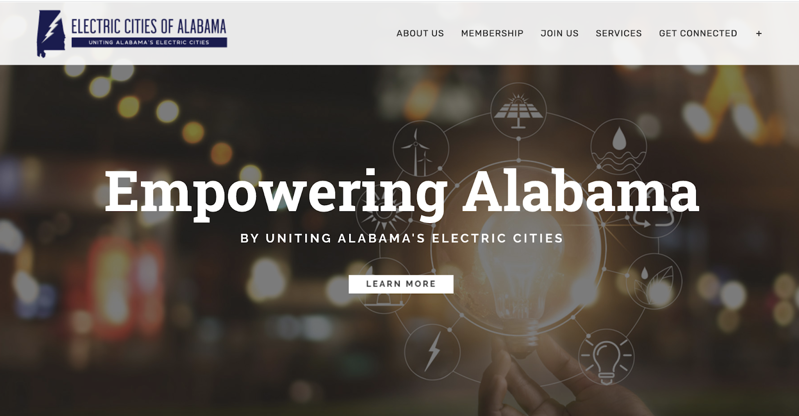 Electric Cities of Alabama homepage showing text overlaid on an evocative image of a bright lightbulb being held against city lights at night.