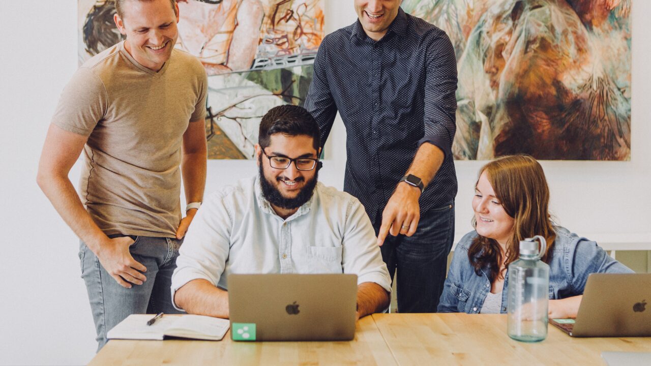 Several smiling people gather around a laptop to build a membership website.