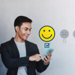 
                            A businessman experiencing a good member experience smiles at the phone he holds while it emits a smiley face icon.                            