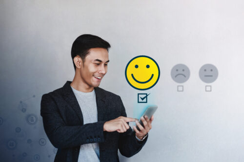 A businessman experiencing a good member experience smiles at the phone he holds while it emits a smiley face icon.