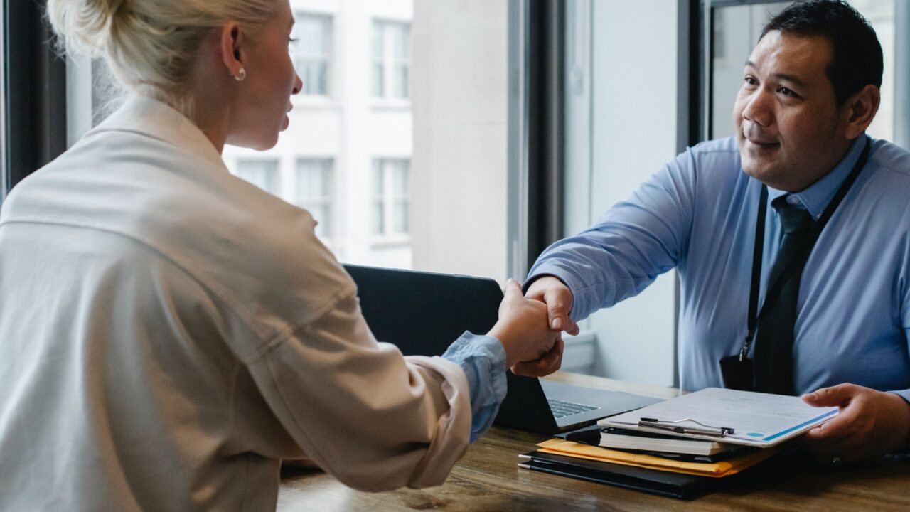 Two members of an association shake hands over an office desk in an agreement about member benefits.