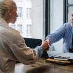 
                            Two members of an association shake hands over an office desk in an agreement about member benefits.                            