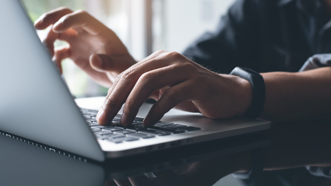 Casual business man hand, hipster, freelance browsing internet, typing on keyboard, busy working on laptop computer, online working concept, close up, backlit, dark tone